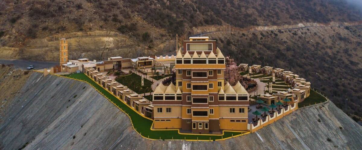 A large, multi-tiered building complex with a central tower, surrounded by a mountainous landscape.