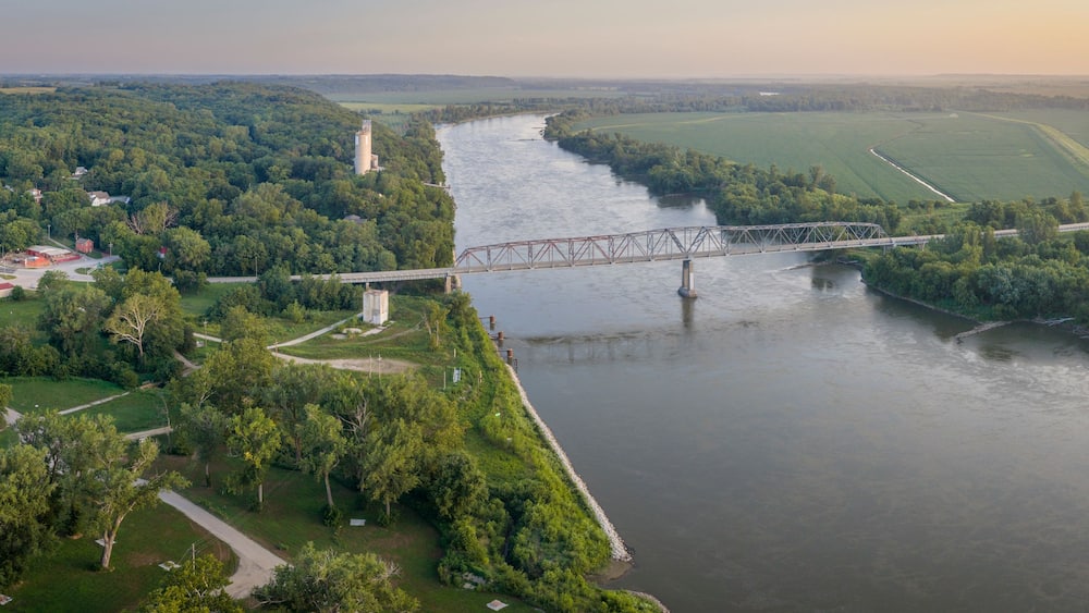 Ein Fluss mit einer Brücke, umgeben von üppigem Grün und Feldern.