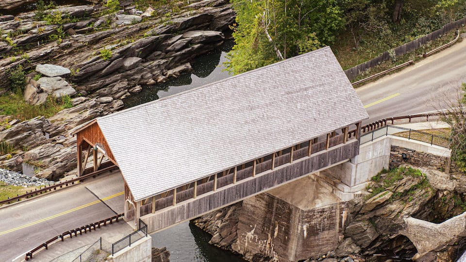 A covered wooden bridge over a river, surrounded by rocky terrain and greenery.