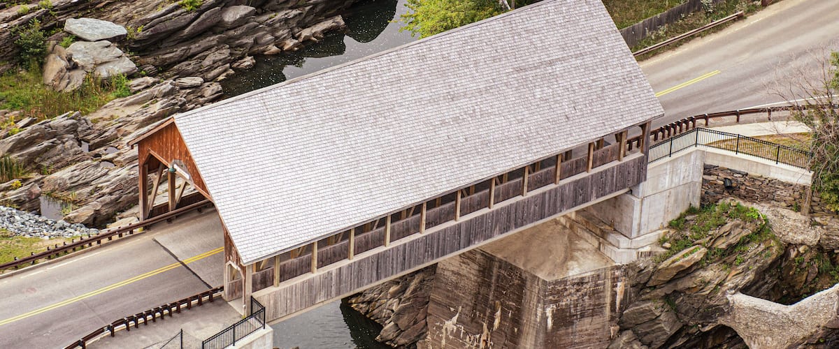 A covered wooden bridge over a river, surrounded by rocky terrain and greenery.