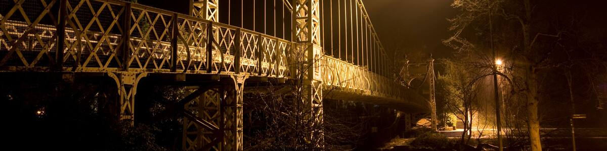 A nighttime view of a large, illuminated bridge with intricate metalwork and a prominent arch.