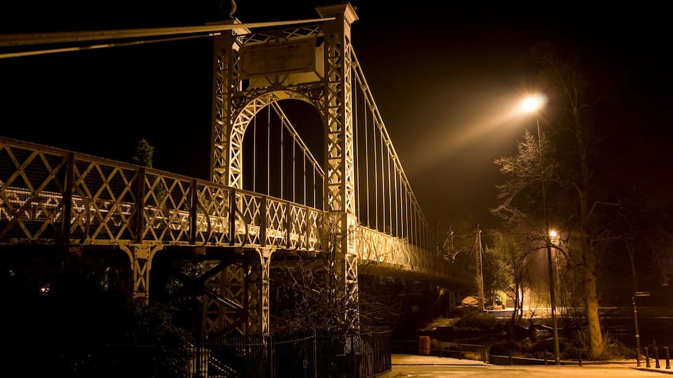 A nighttime view of a large, illuminated bridge with intricate metalwork and a prominent arch.