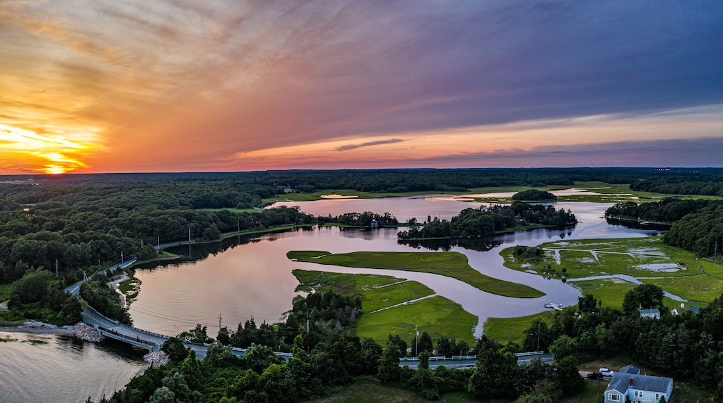 A sunset over a river with a bridge, surrounded by greenery and a small house.