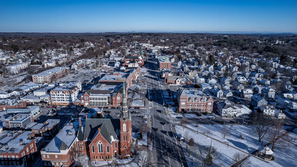 An aerial view of a town with snow-covered streets, a prominent church, and residential houses.