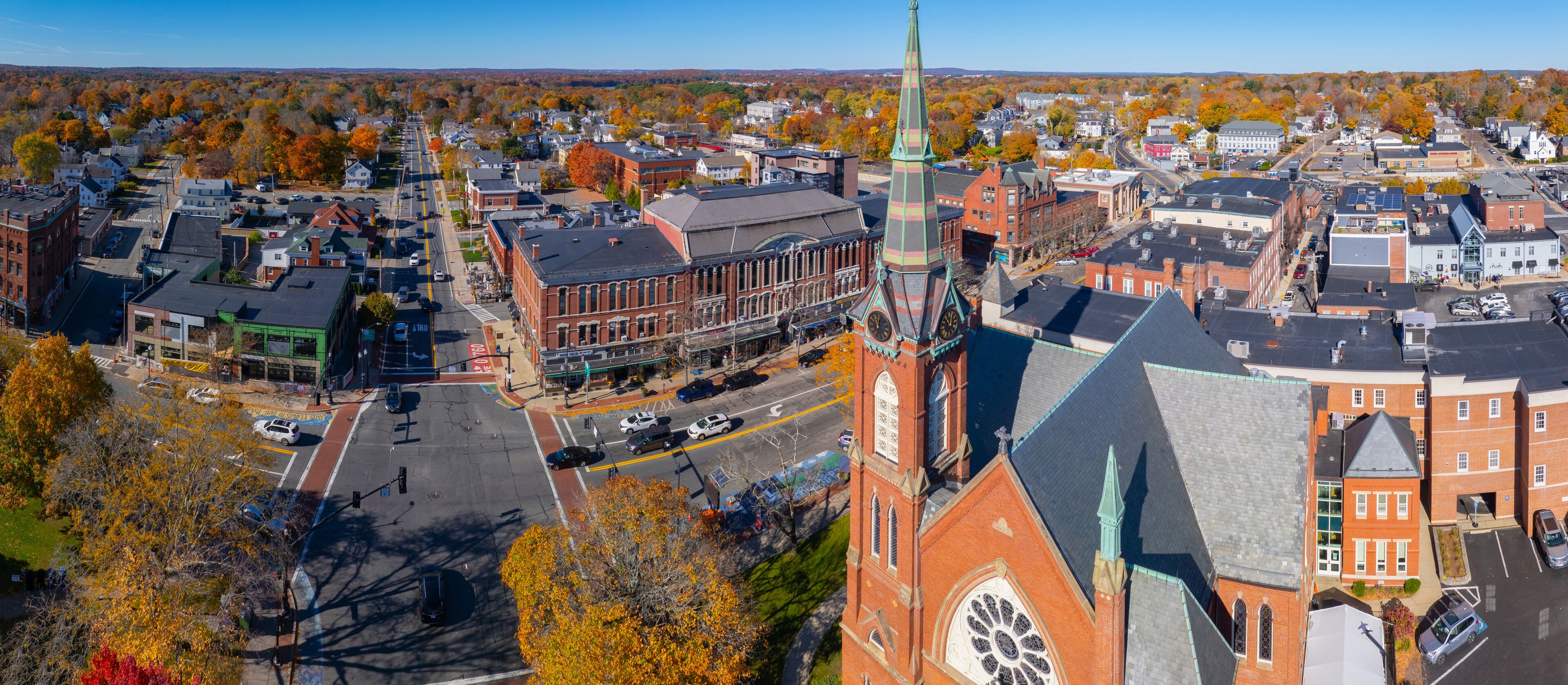 An aerial view of a town with a prominent church steeple, a main street, and autumn-colored trees.