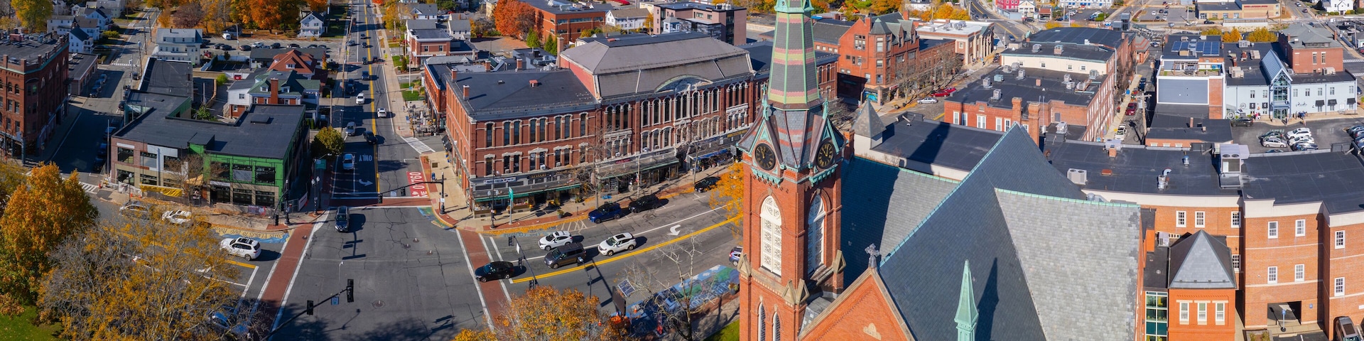 An aerial view of a town with a prominent church steeple, a main street, and autumn-colored trees.