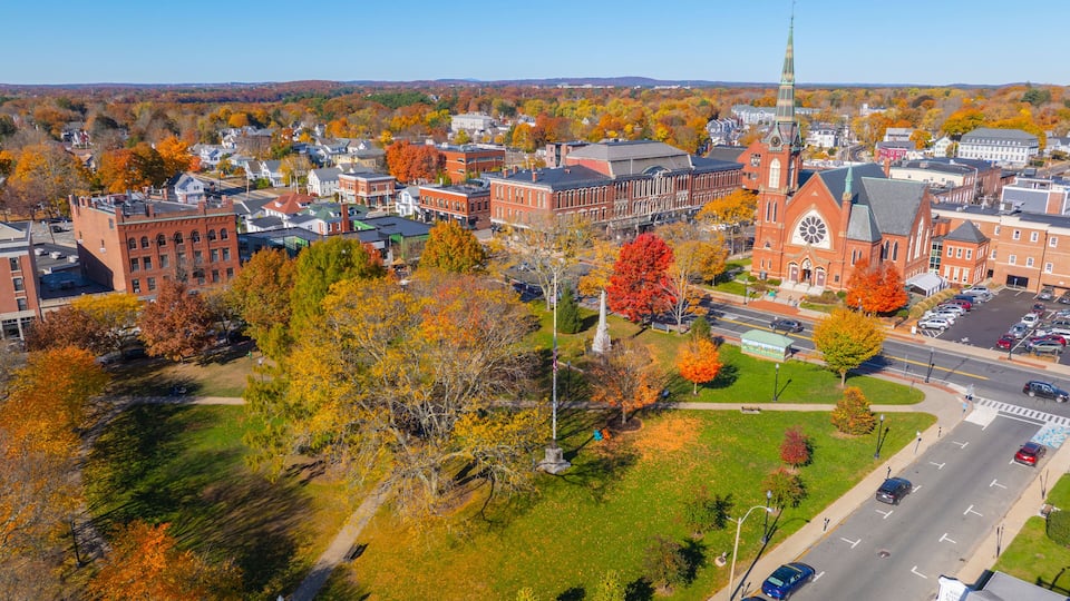 A town with autumn foliage, a prominent church with a clock tower, and a mix of residential and commercial buildings.