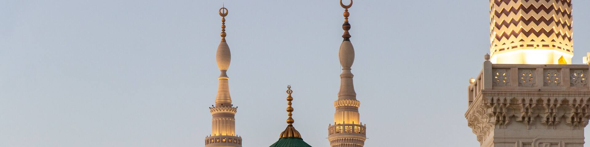 A mosque with a green dome and three minarets.