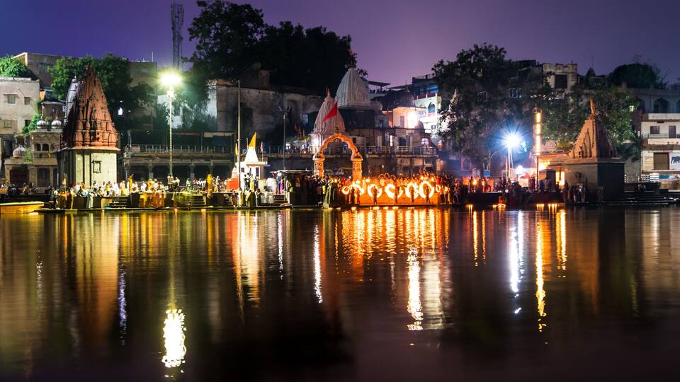 A nighttime view of a riverside with illuminated structures and a crowd gathered near the water.