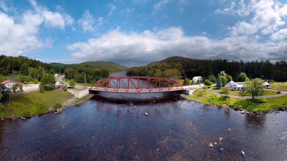 A red bridge over a river with houses and greenery on both sides.