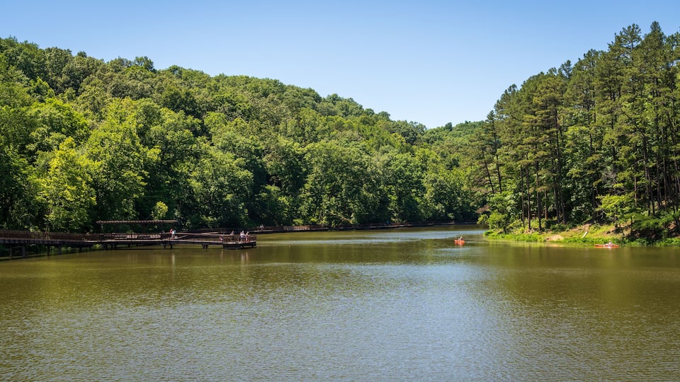 A calm lake surrounded by dense forest, a wooden dock, and a small boat.