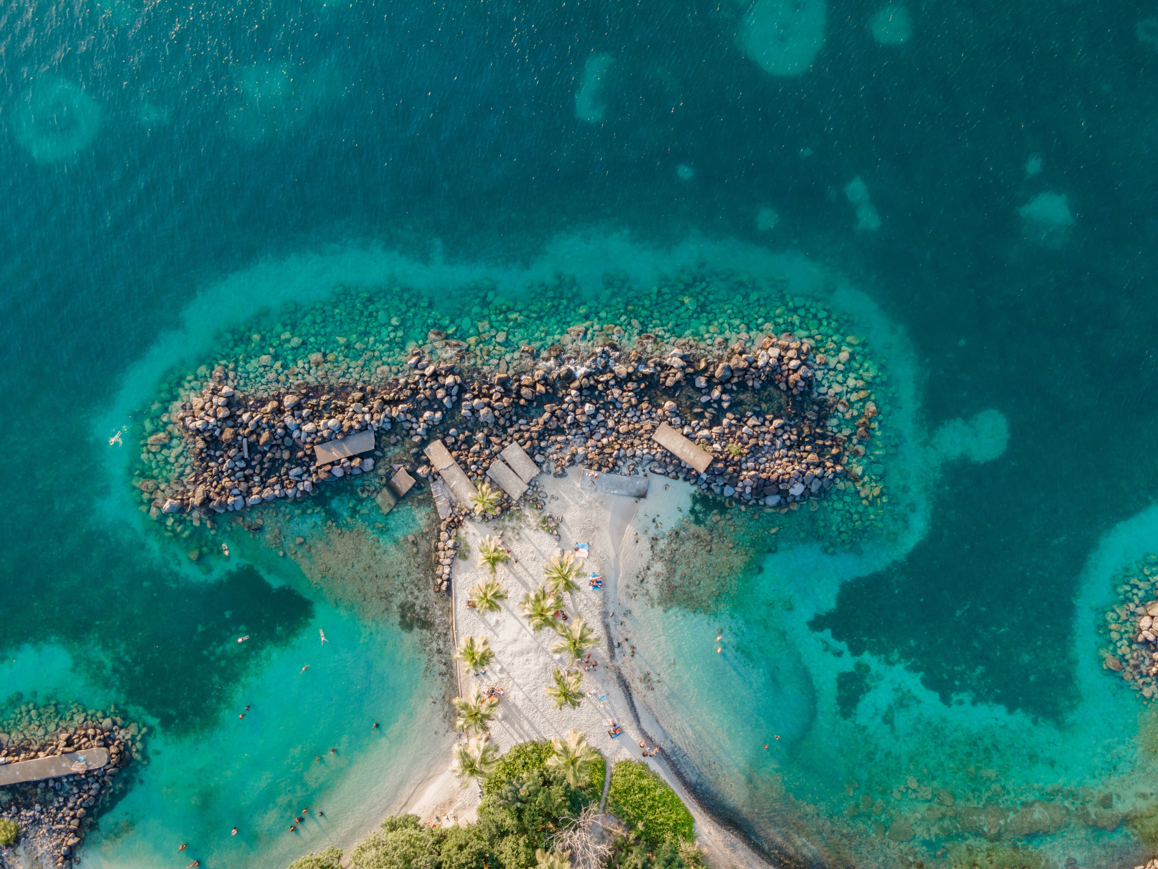 An aerial view of a tropical island with clear turquoise waters, a sandy beach, and scattered palm trees.