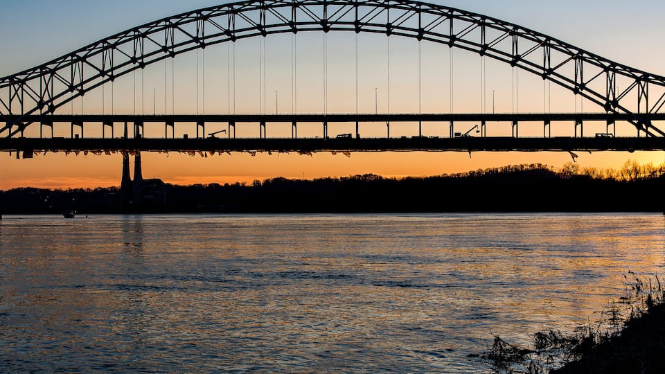 A large steel bridge arching over a body of water at sunset.