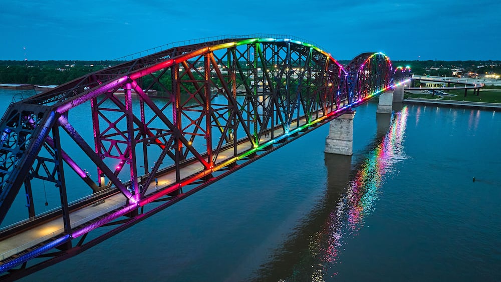 Arch bridge aerial rainbow pride illuminated at night with reflected colors in water over Ohio River