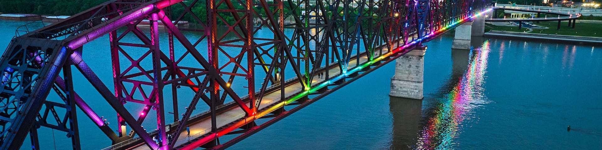 A brightly lit bridge with a rainbow of lights reflecting on the water.