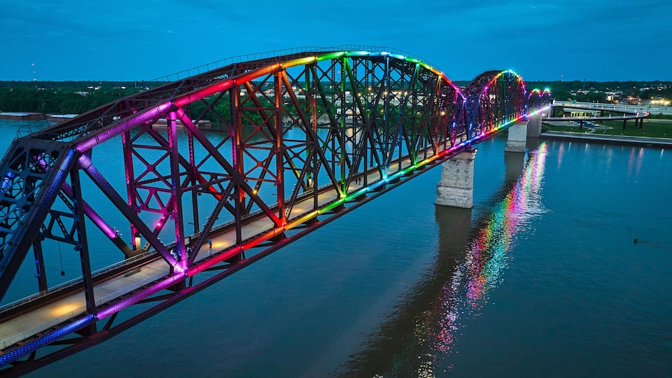 A brightly lit bridge with a rainbow of lights reflecting on the water.