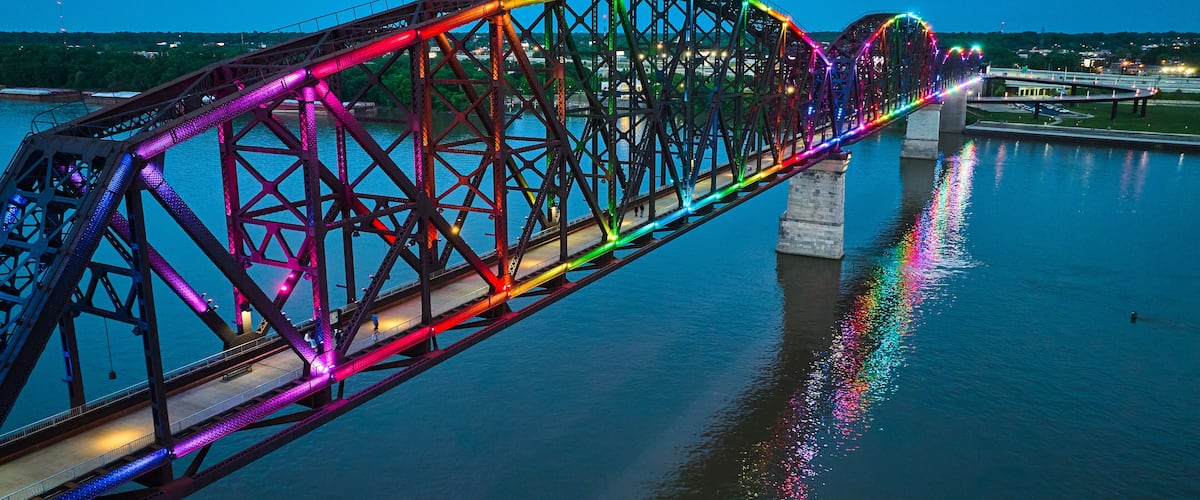 A brightly lit bridge with a rainbow of lights reflecting on the water.