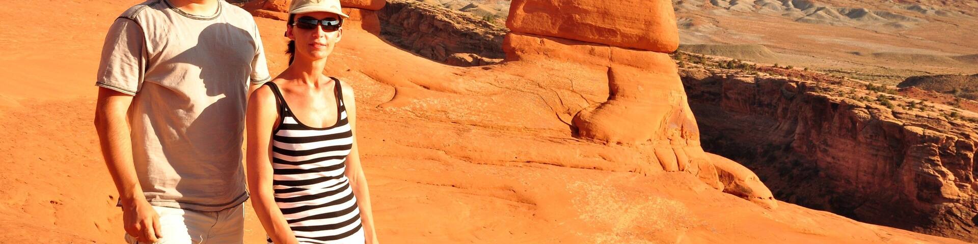 A couple standing in front of a natural rock arch formation with a desert landscape in the background.