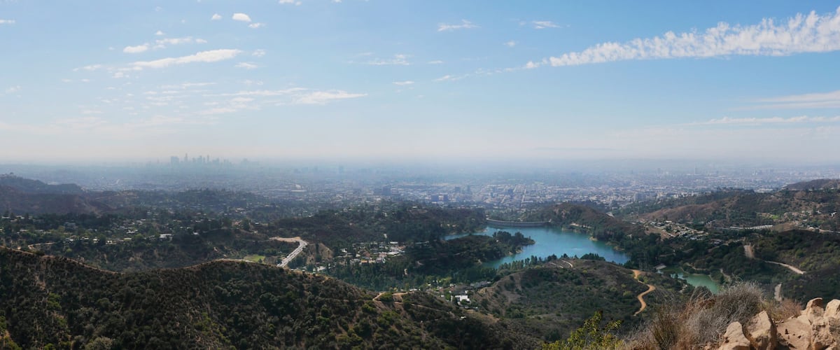 A mountainous landscape with a lake, a city in the distance, and a tall communication tower.