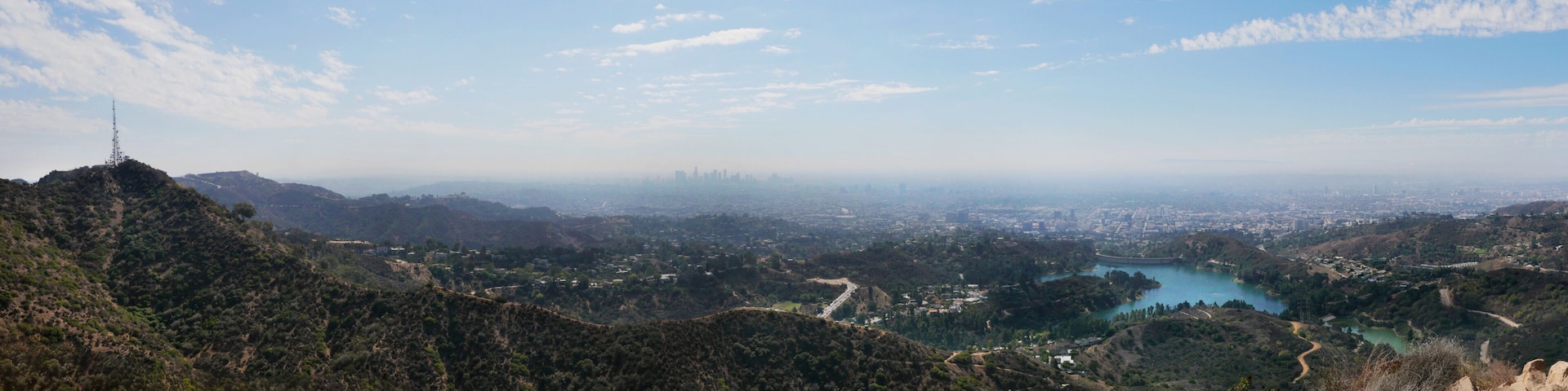 A mountainous landscape with a lake, a city in the distance, and a tall communication tower.