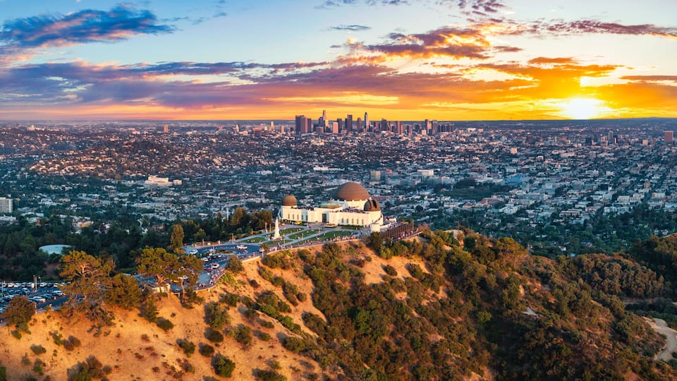 A cityscape with a prominent dome-shaped building surrounded by hills and a sunset sky.