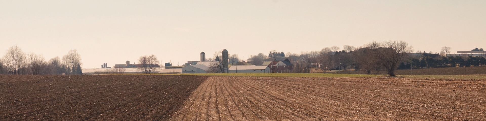 Rows of Winter Fields Leading to Farm Buildings with Blue Sky