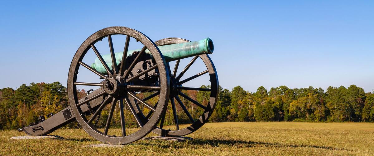 A cannon in a grassy field with trees in the background.