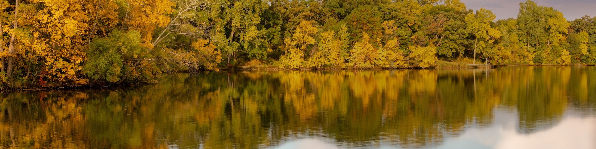 A calm lake with autumn foliage reflecting in the water, surrounded by dense trees.