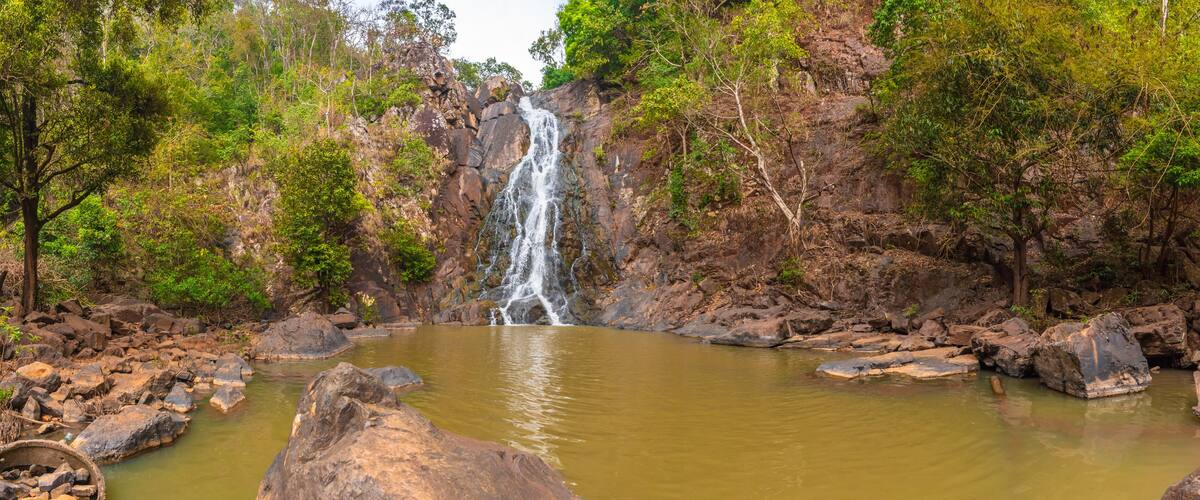 A waterfall cascading into a calm pool surrounded by rocky terrain and dense foliage.