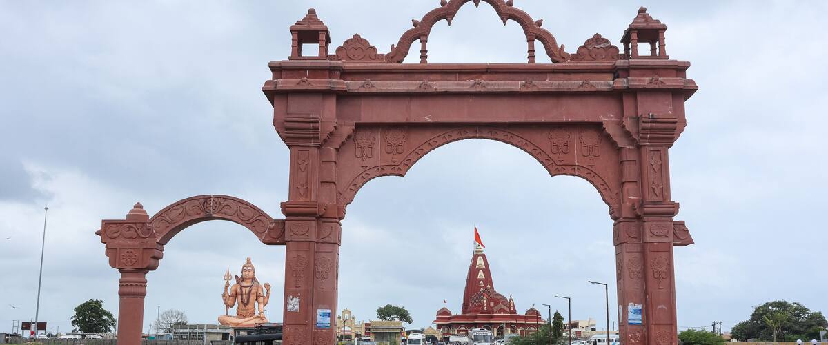 A large red archway with intricate carvings, leading to a temple with a spire.
