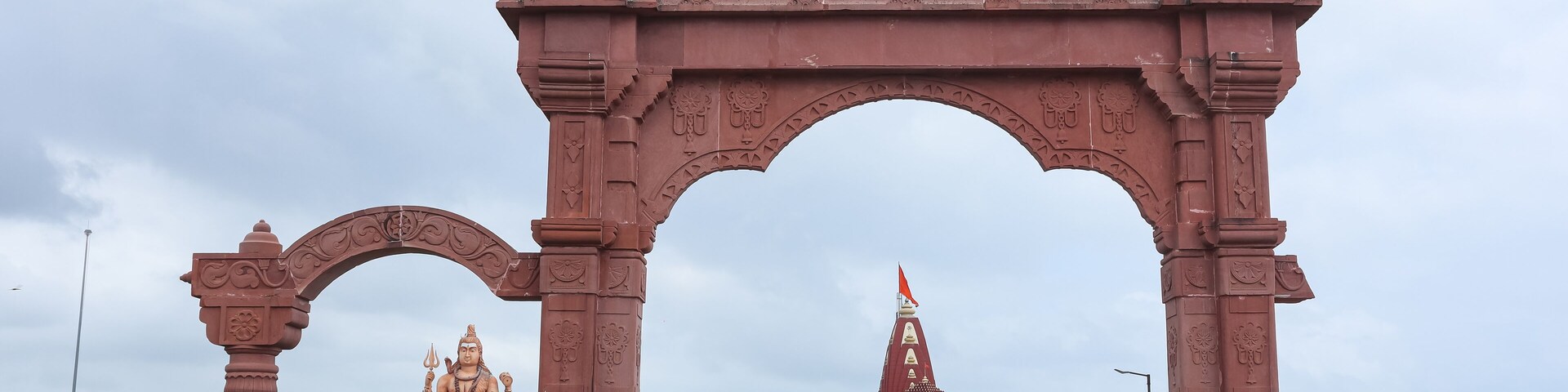 A large red archway with intricate carvings, leading to a temple with a spire.
