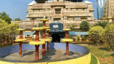 A temple with a large central dome, intricate carvings, and a surrounding water feature with stone pillars.