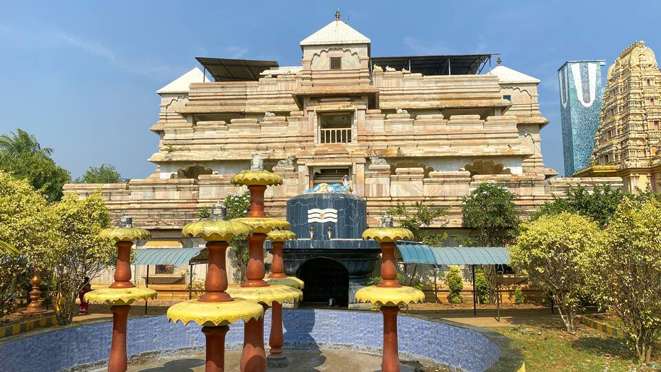 A temple with a large central dome, intricate carvings, and a surrounding water feature with stone pillars.