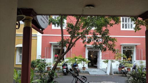 Vista de una calle con un edificio rojo, plantas en macetas y motocicletas estacionadas.