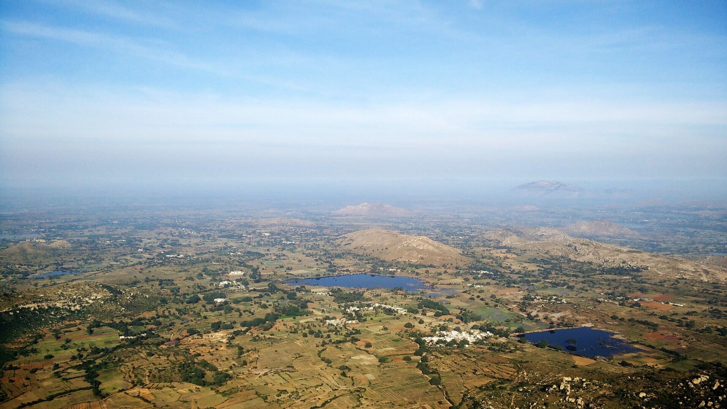 A vast landscape with rolling hills, scattered fields, and several small lakes.