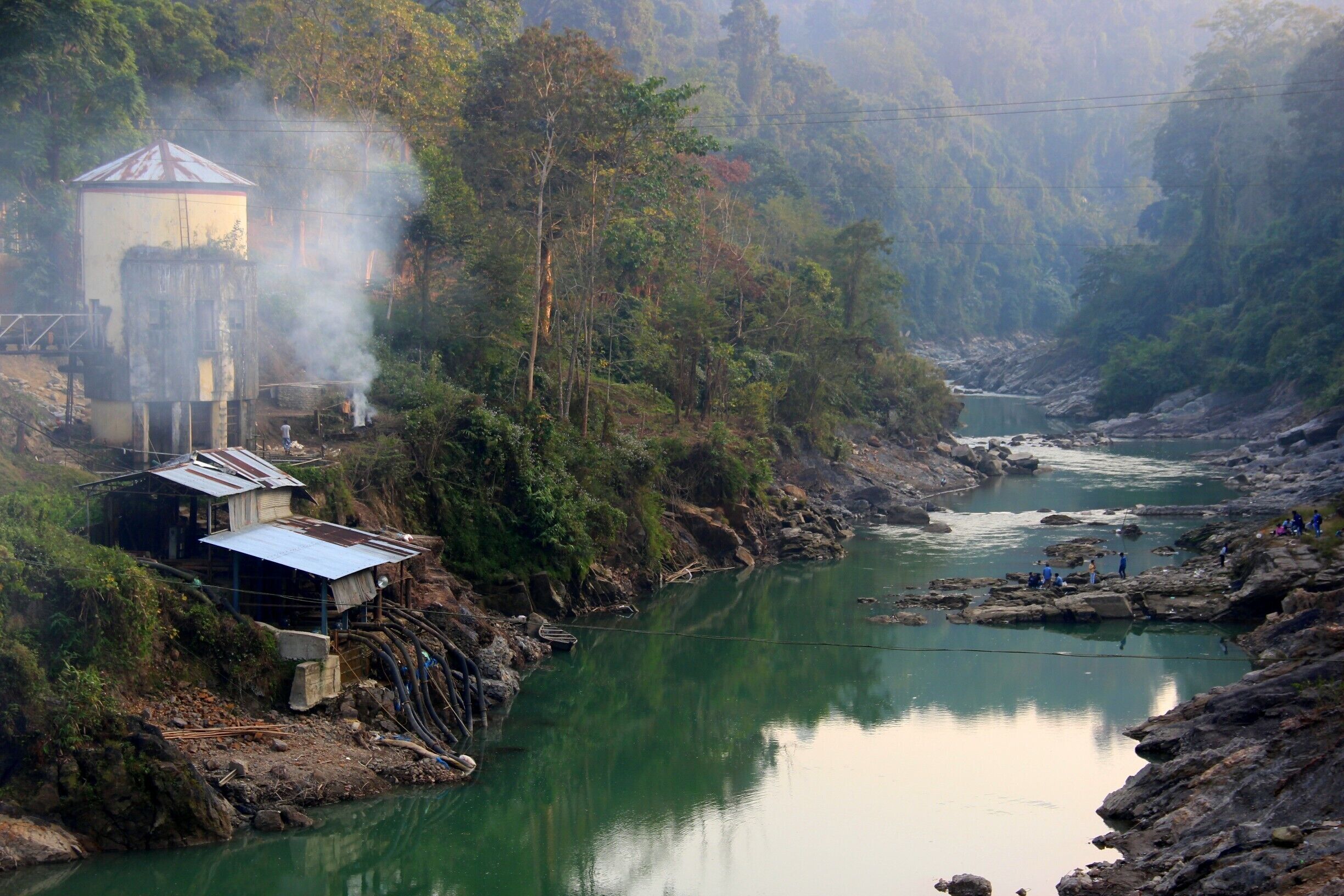 A river with a small dam and houses on the left bank.