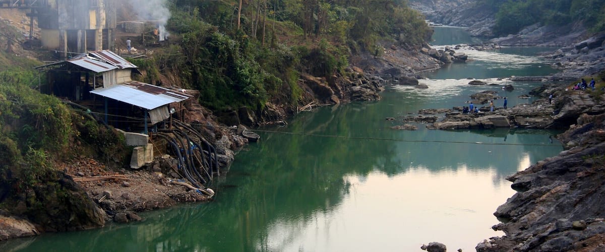 A river with a small dam and houses on the left bank.