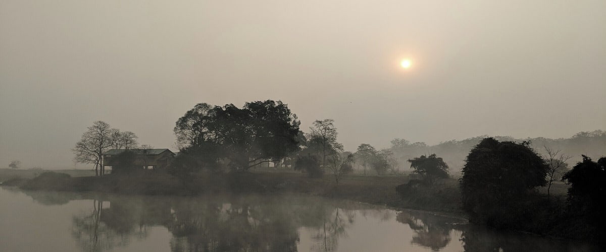 A misty landscape with a calm body of water reflecting trees and a house.