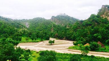 A lush green valley with terraced fields, a winding river, and a small traditional hut.