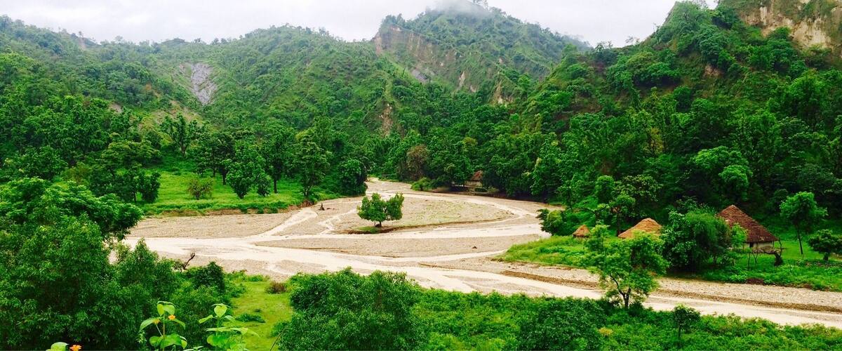 A lush green valley with terraced fields, a winding river, and a small traditional hut.