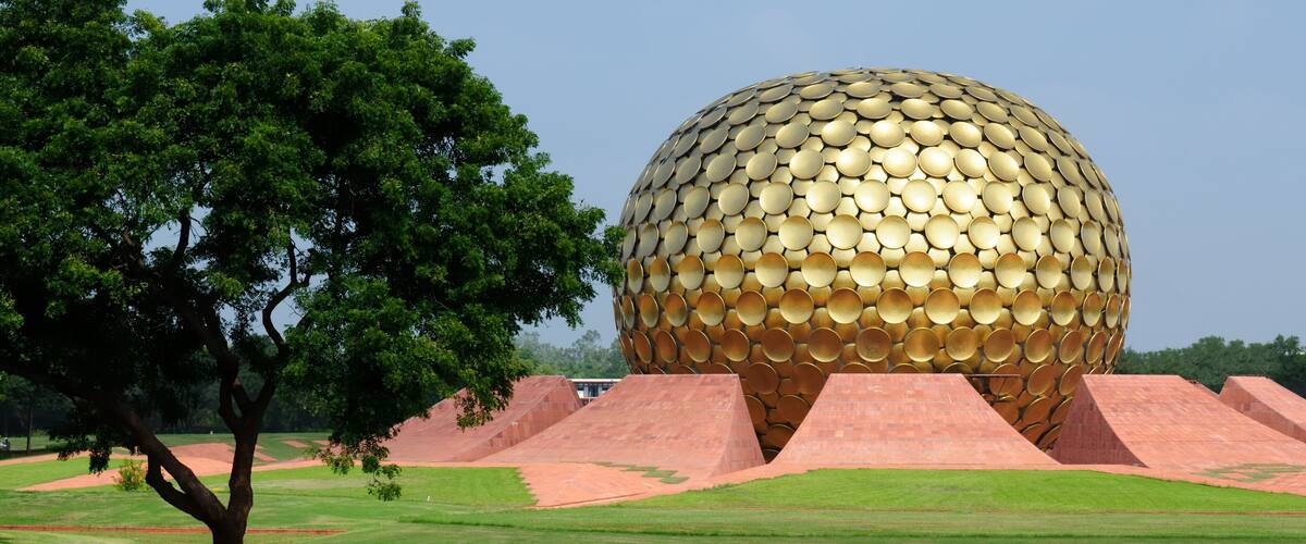 A large golden sphere with a pattern of circular panels, surrounded by red pyramids and a green field with a tree.