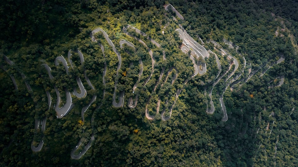 An aerial view of a winding road through a dense forest.