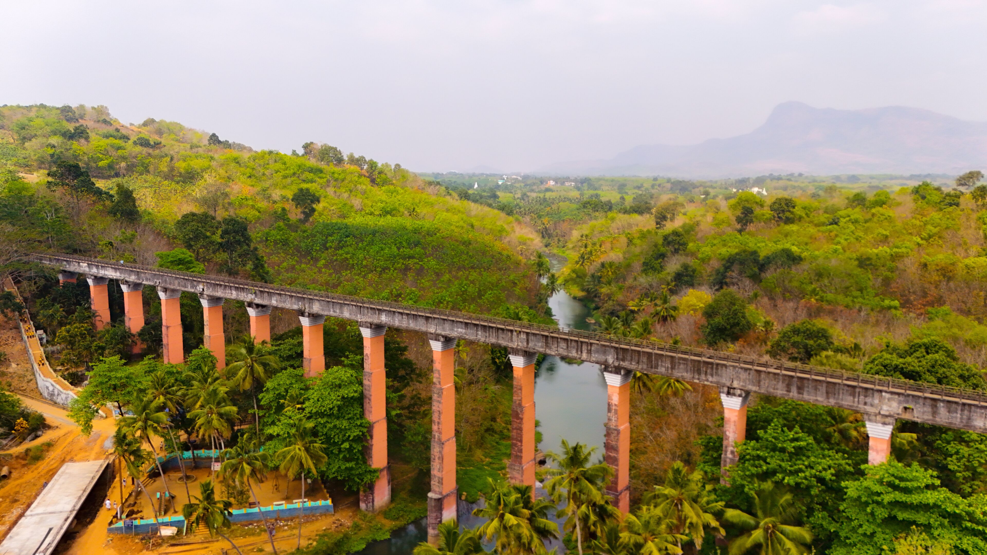 A bridge over a river with surrounding greenery and hills.