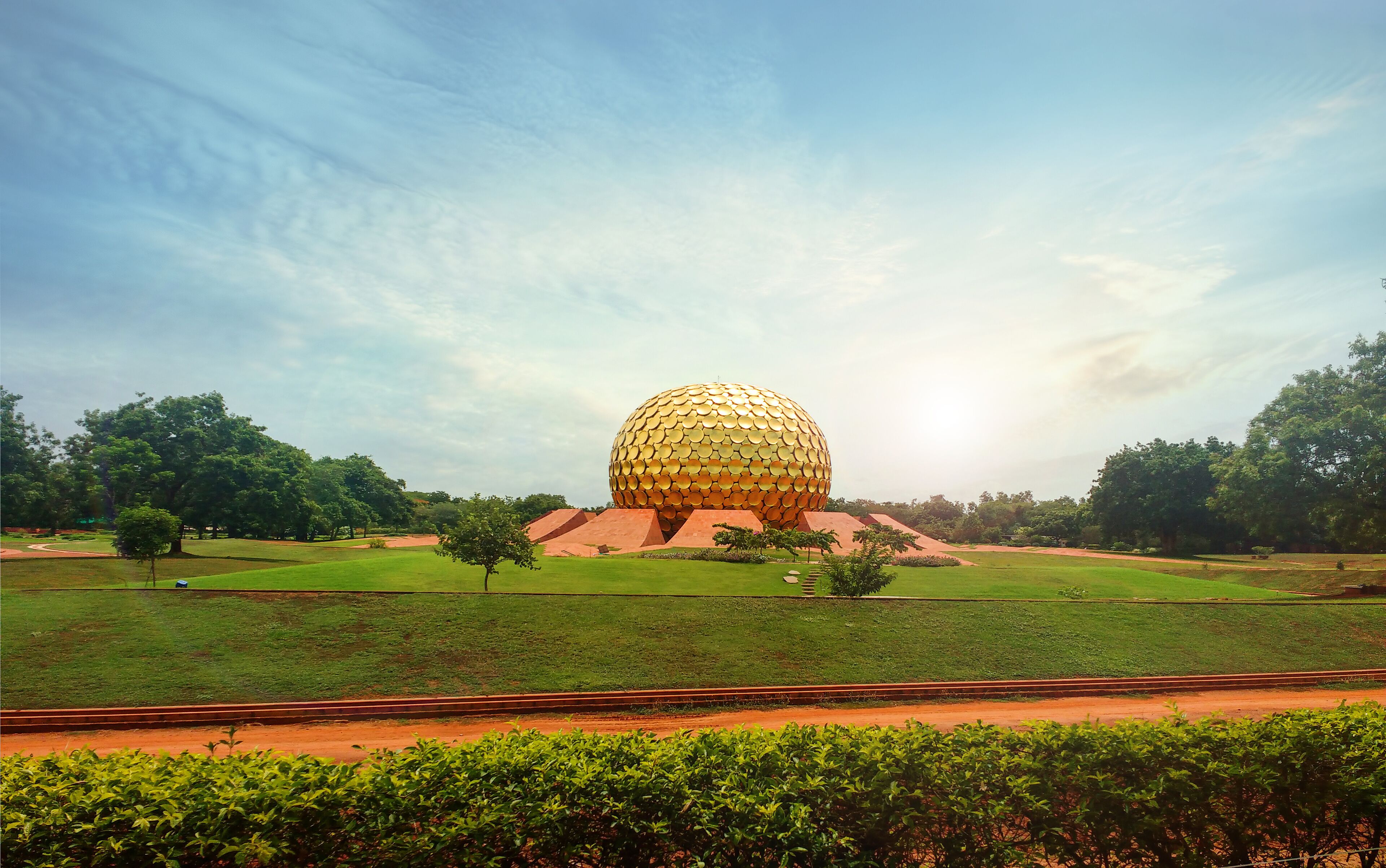 A large golden sphere structure surrounded by green grass and trees.