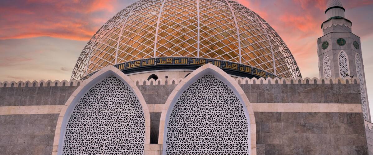 A large dome with intricate patterns and a minaret with clocks.
