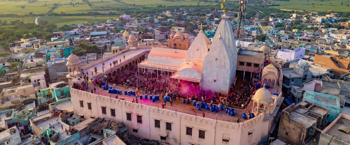 A large temple complex surrounded by densely packed buildings, with a crowd gathered in the central courtyard.