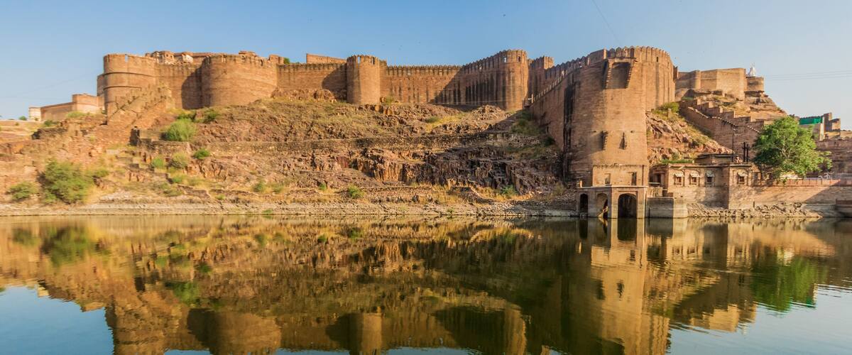 A historic fort with a reflection in the water, surrounded by hills.