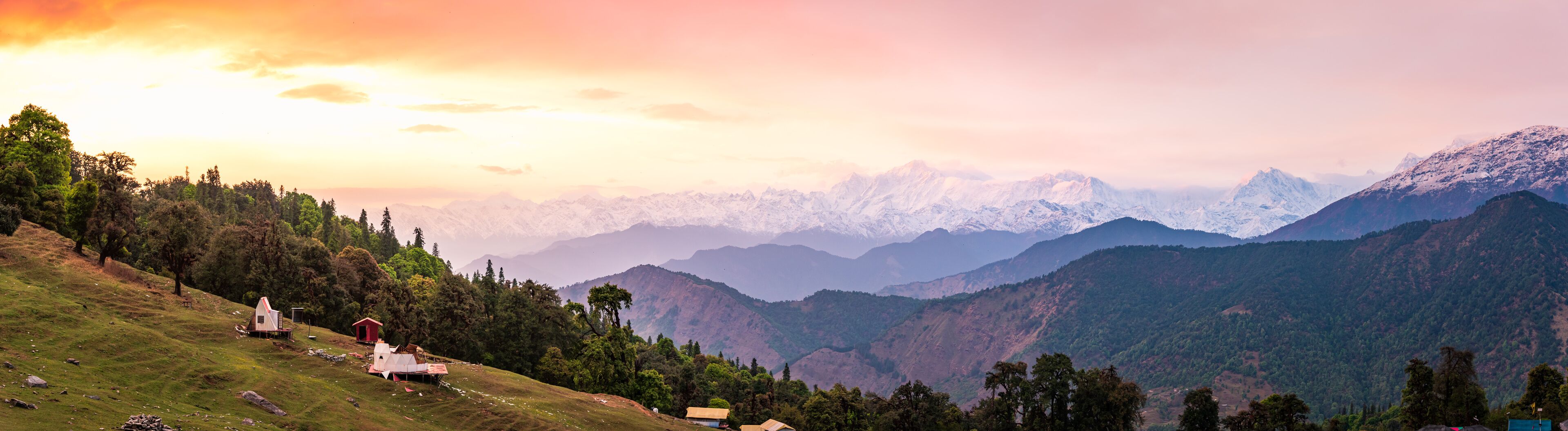 A mountainous landscape with a sunrise, snow-capped peaks, and scattered buildings.