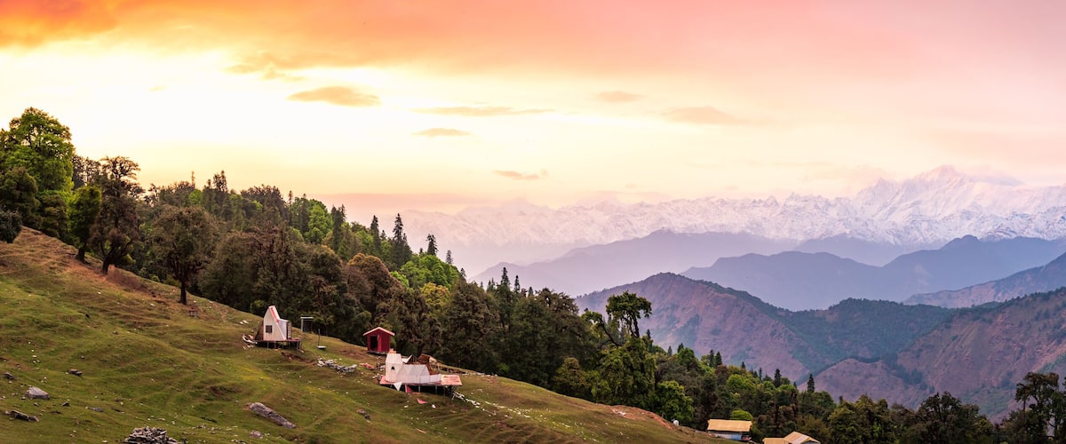 A mountainous landscape with a sunrise, snow-capped peaks, and scattered buildings.