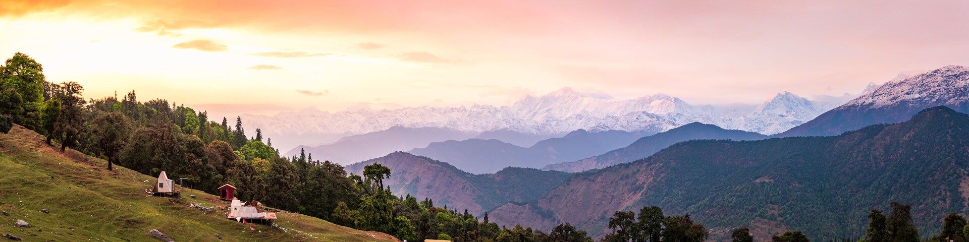 A mountainous landscape with a sunrise, snow-capped peaks, and scattered buildings.